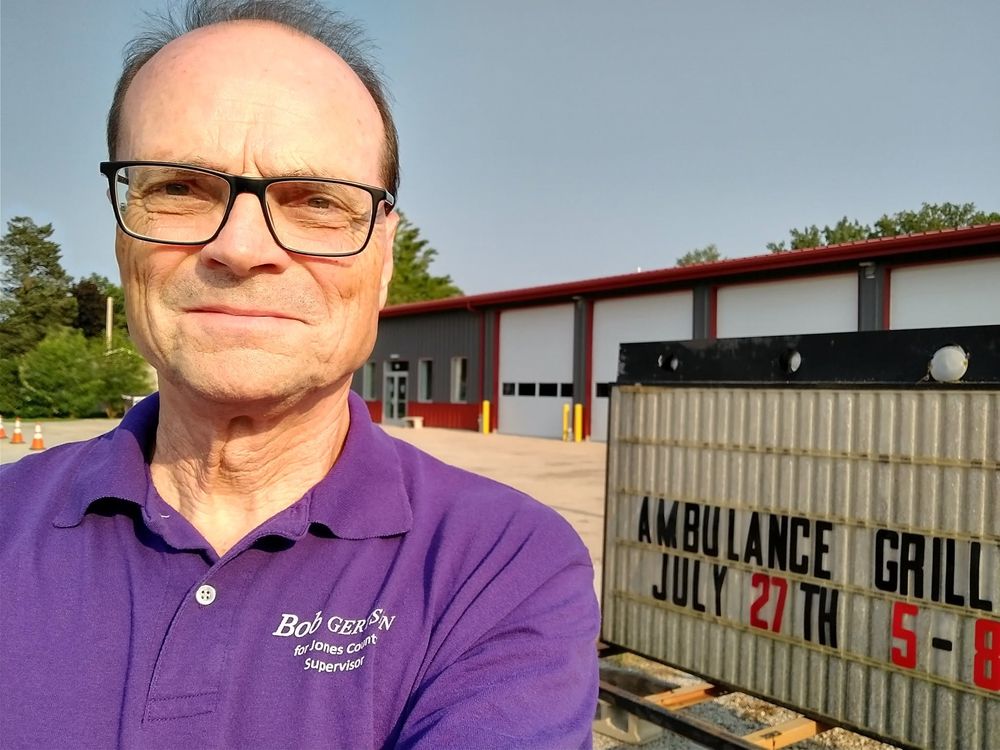 Bob Gertsen beside a sign for an ambulance department grill fundraiser